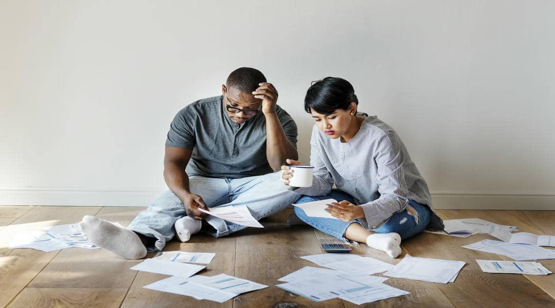 Worried Couple Reviewing Finances on Wooden Floor